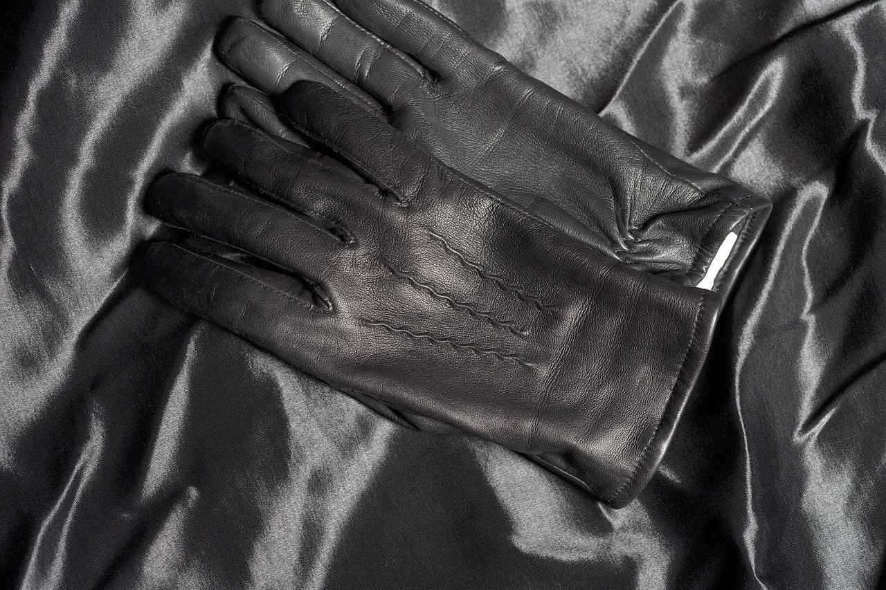 Pair of brown leather gloves laid flat on a white surface with visible stitching details.

